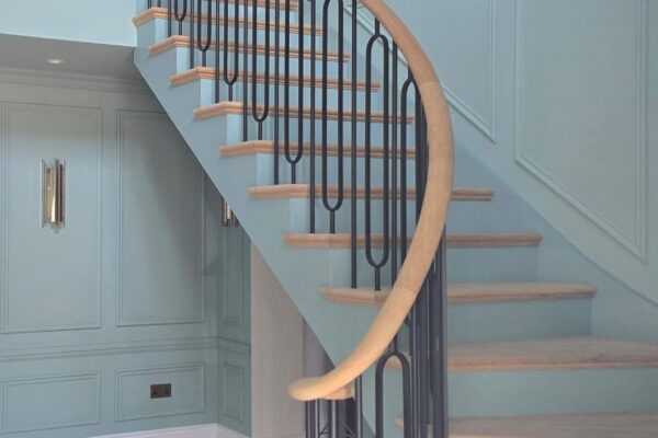 Bespoke curved oak staircase with iron balustrade in a panelled hallway