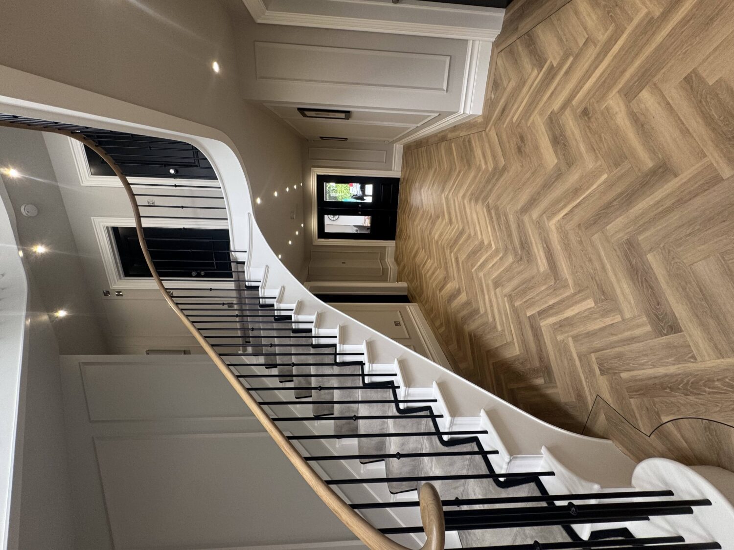Curved staircase with painted string and solid oak handrail sweeping down to a herringbone floor in a private house