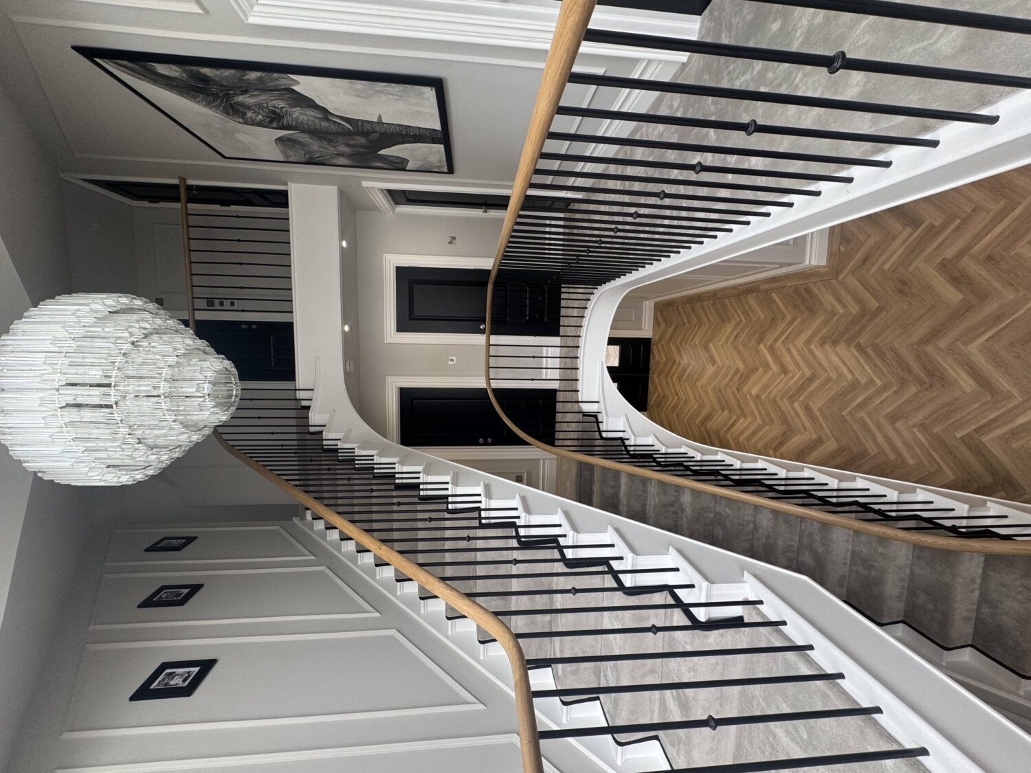 Curved staircase rising to a galleried landing, with oak handrail and slim black metal spindles