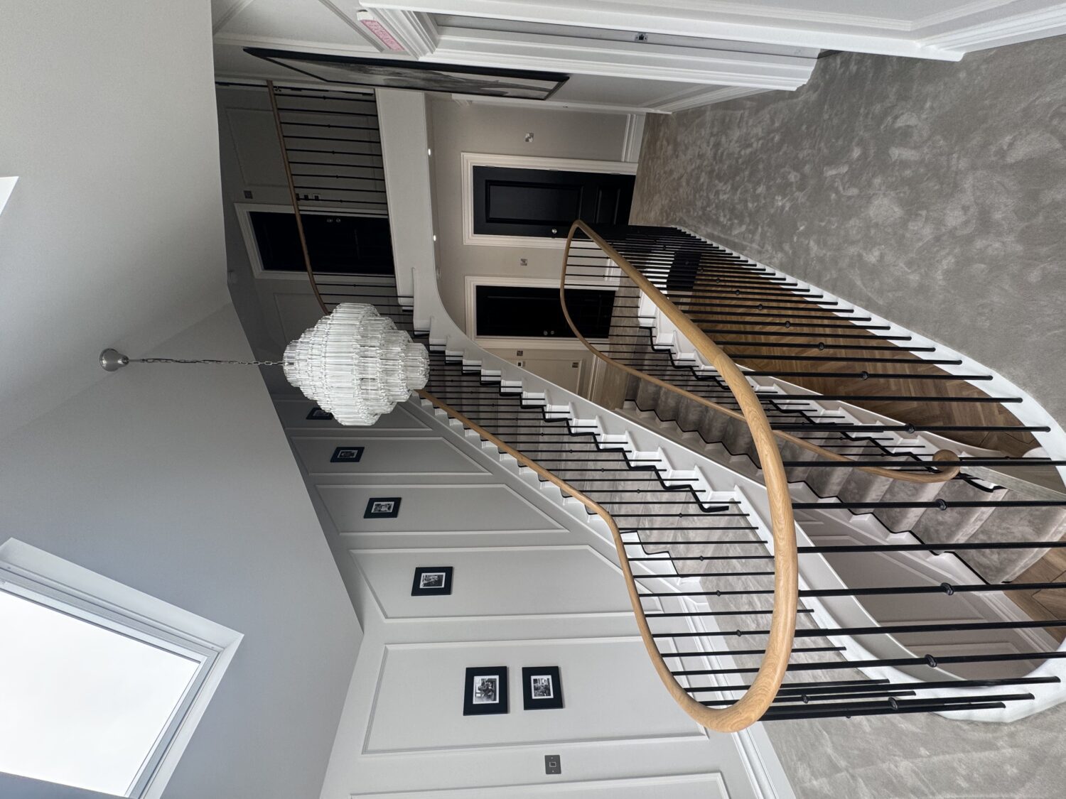 Curved oak handrail and black metal spindles to a first floor landing beneath a vaulted rooflit ceiling