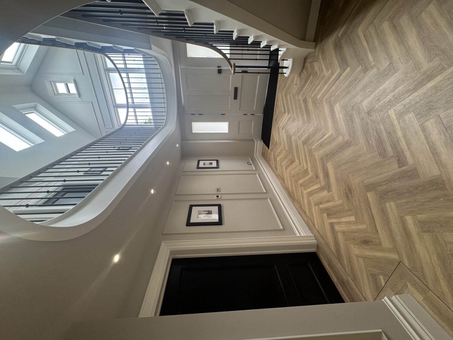 Entrance hall with a curved staircase and oak handrail rising beneath a double height rooflit ceiling void