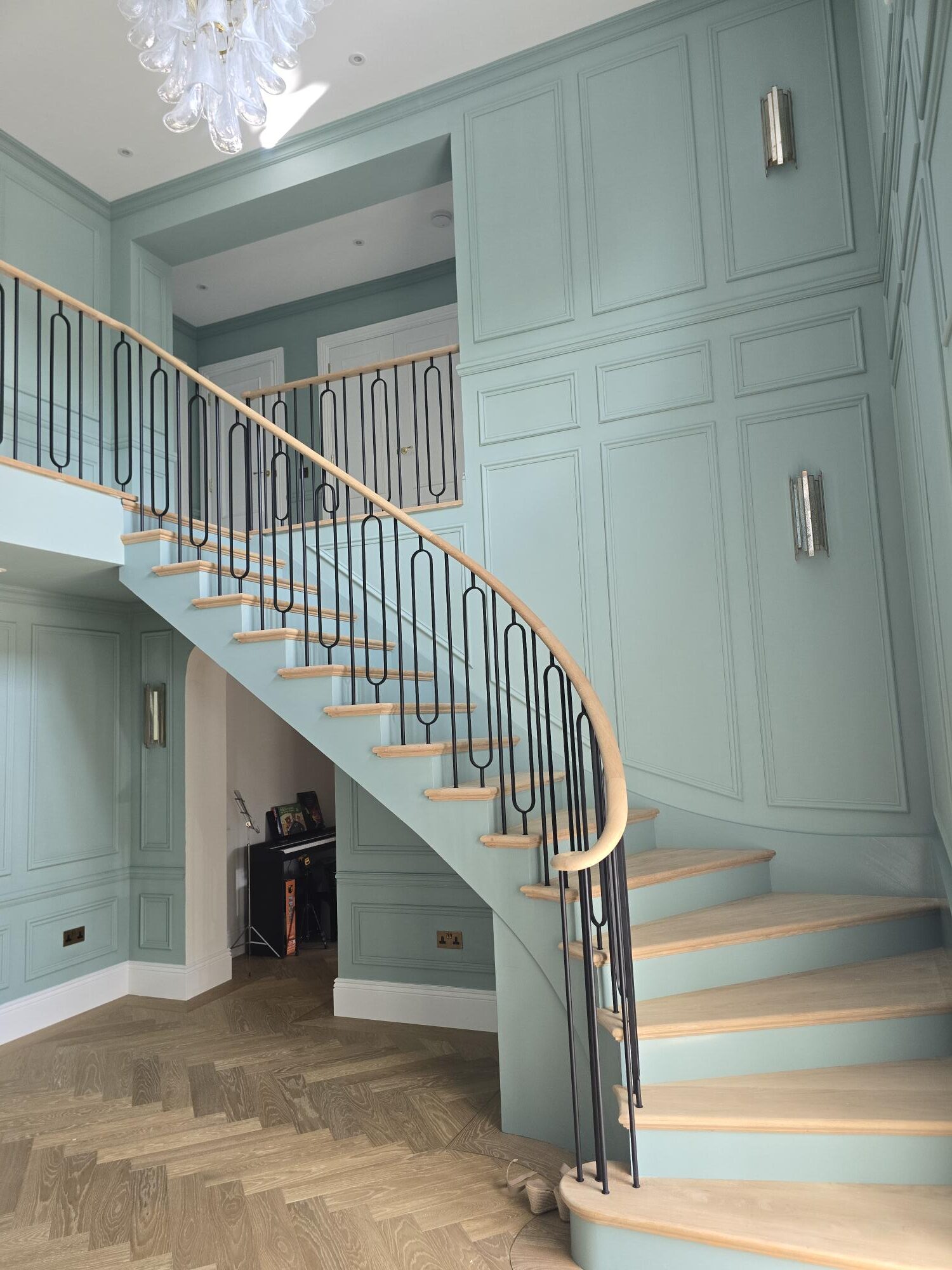 Bespoke curved oak staircase with iron balustrade in a panelled hallway