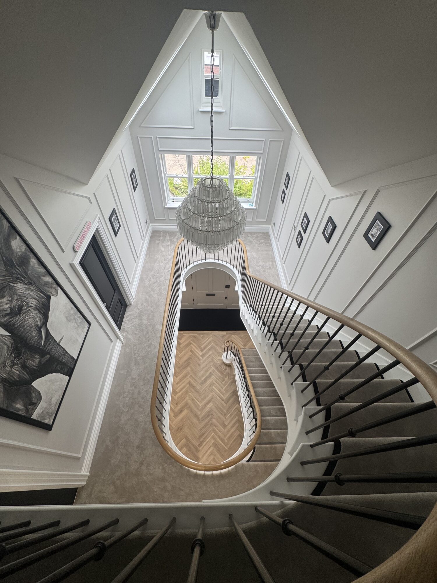 Looking down through the stairwell at a curved staircase with a chandelier and roof lights, Roundwood Grove
