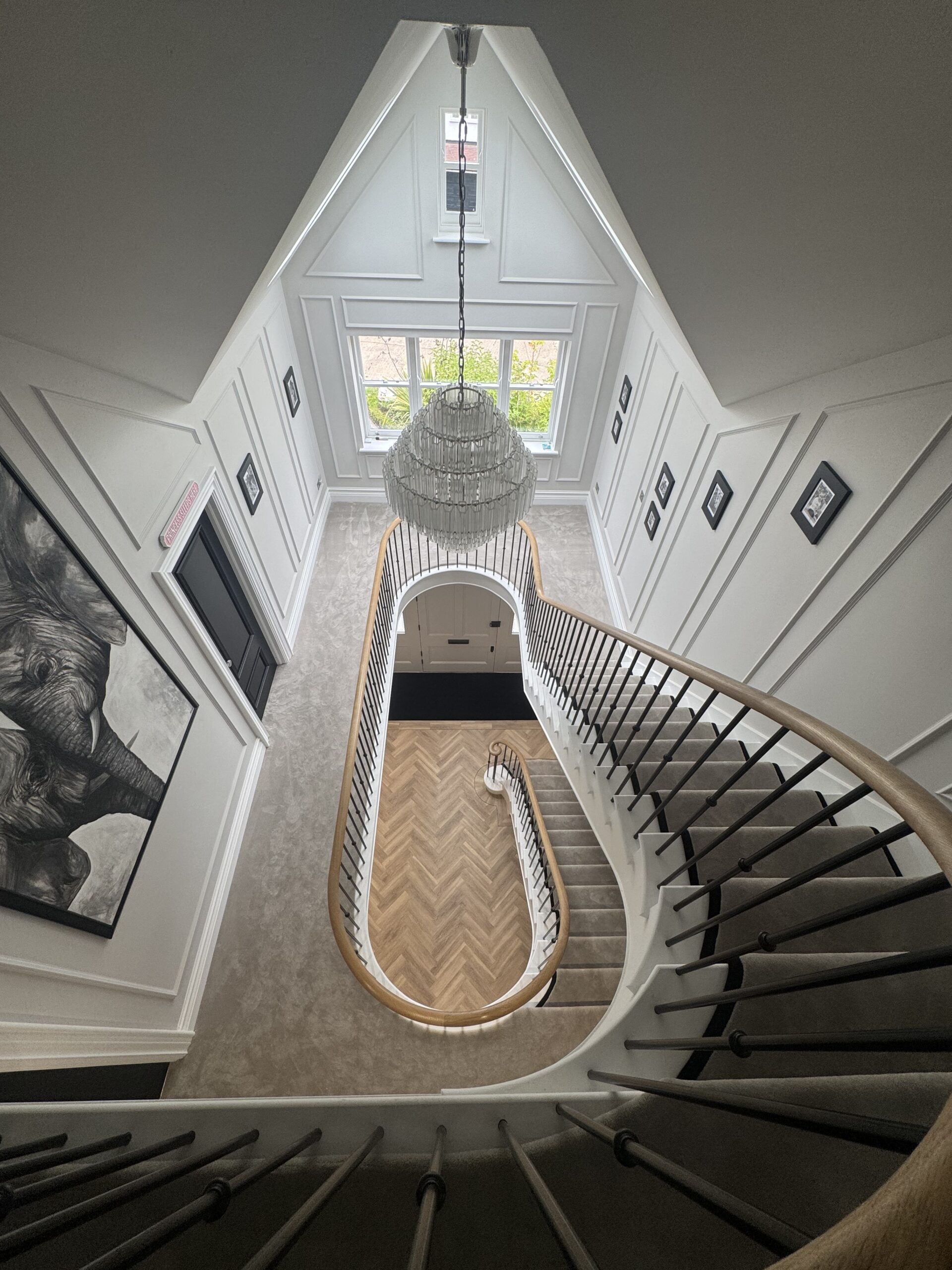 Looking down through the stairwell at a curved staircase with a chandelier and roof lights, Roundwood Grove